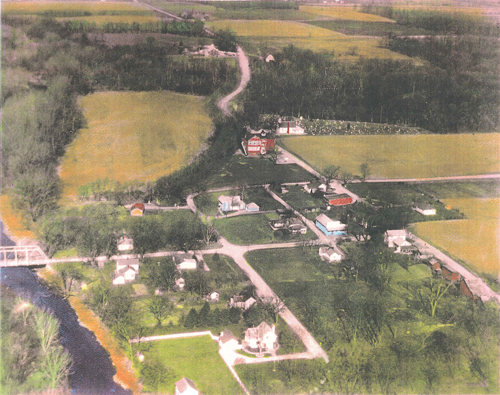 A hand-colored aerial photo shows Monument City prior to 1964, looking from east to west (bottom to top) and south to north (left to right). The Salamonie River is on the far left. The red school building, white Wesleyan Church and cemetery are at top right. Town photos courtesy of Rowena Richardson
