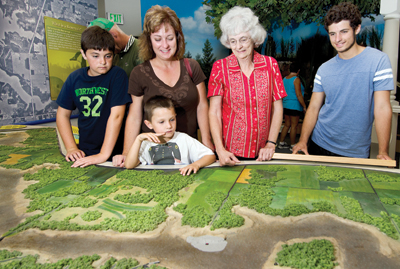 The Salamonie Interpretive Center offers a 3D map of the reservoir. Looking over the Monument City site (the gray area with the red light) is Nancy Smith who was married in Monument City 58 years ago. With her are her daughter, Anita Hughes, and grandsons, from left, Maxwell, Jackson and Alex.