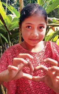 After watching Indiana linemen climb poles and string wire in her village, a Guatemalan girl forms a heart with her fingers as an expression of gratitude toward the Americans who came to change their lives. Photo by Diane Willis