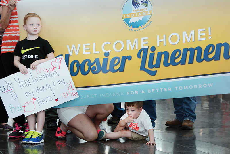 Scores of family and co-op co-workers greeted the linemen as they arrived at Indianapolis International Airport with signs, hugs and kisses after the two-week trip. Among those anxiously waiting for the group to emerge beyond the security gates are Lukas Shirley, left, and his little brother, Gunner, sons of Boone REMC lineman Michael Shirley. Photo by Richard G. Biever