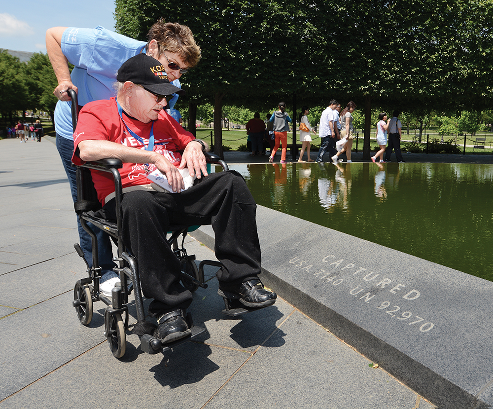 1:19 pm: Raymond Turpen, one of the two Korean War veterans on the Honor Flight, and his guardian, Sue Gipson, pause before the Pool of Remembrance at the Korean War Veterans Memorial. At their feet, the memorial notes the numbered captured, “U.S.A. 7,140.” Turpen was visibly touched; he was one of those 7,140 during the war that was waged from June 1950 to July 1953.