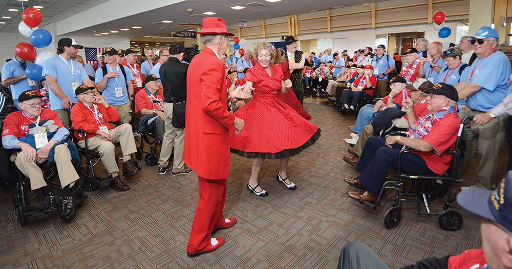 6:38 pm: Returning to Reagan National Airport for the flight home, the group is met with more kisses and hugs and entertainers dressed in zoot suits and dresses of the 1940s who danced the jitterbug and more. They rolled with veterans in wheel chairs and danced with others.