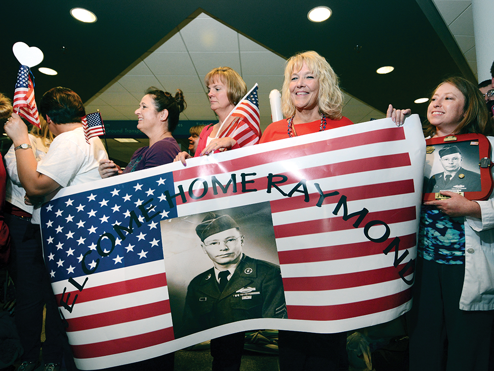 9:41 pm: (above) Inside the airport terminal, an estimated 2,000 people create a corridor of cheering, flag waving, applauding and handshaking supporters stretching from the arrival gate to the exit doors. A group of family and friends wait for Honor Flight participant Raymond Turpen to make his way through the well wishers. 