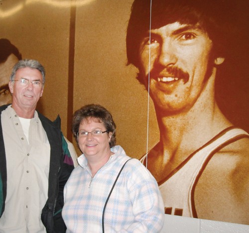 Rick and Cindy Wells stand beside an image of Rick at the War Memorial Coliseum in Fort Wayne. He played basketball at Indiana Tech. But it was softball that brought them together. She was an umpire who called him out at first, a call he disputed, right up until he asked her for a date. 