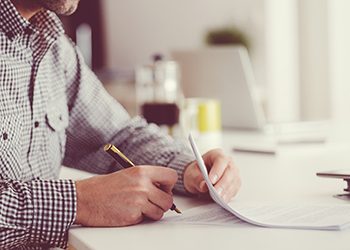 Man sitting at the table, holding a pen and signing contract. Focus on hands, unrecognizable person.