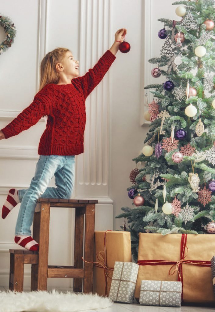 Kid trying to hang a ornament on a Christmas tree