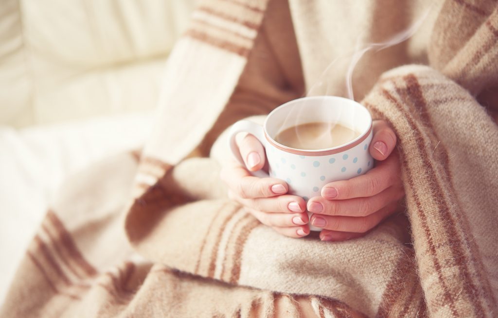 Woman holding a cup of coffee in a blanket