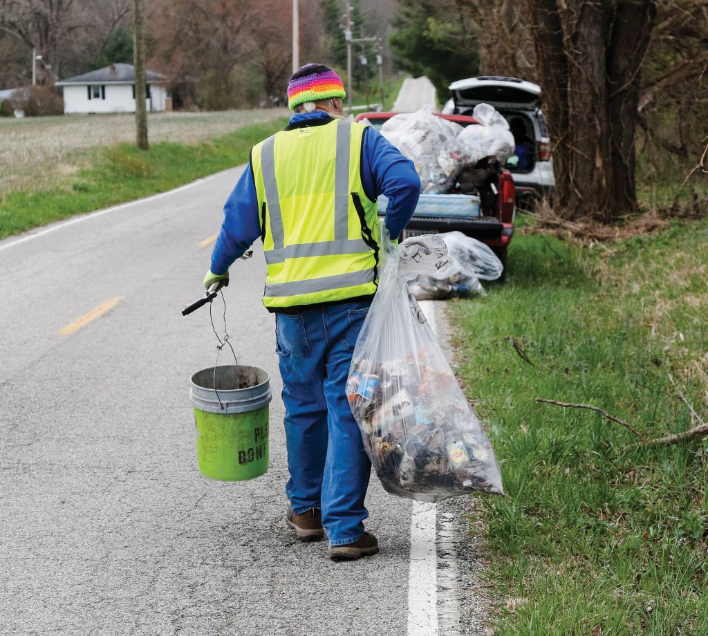 Photo of man picking up trash along the roadside.
