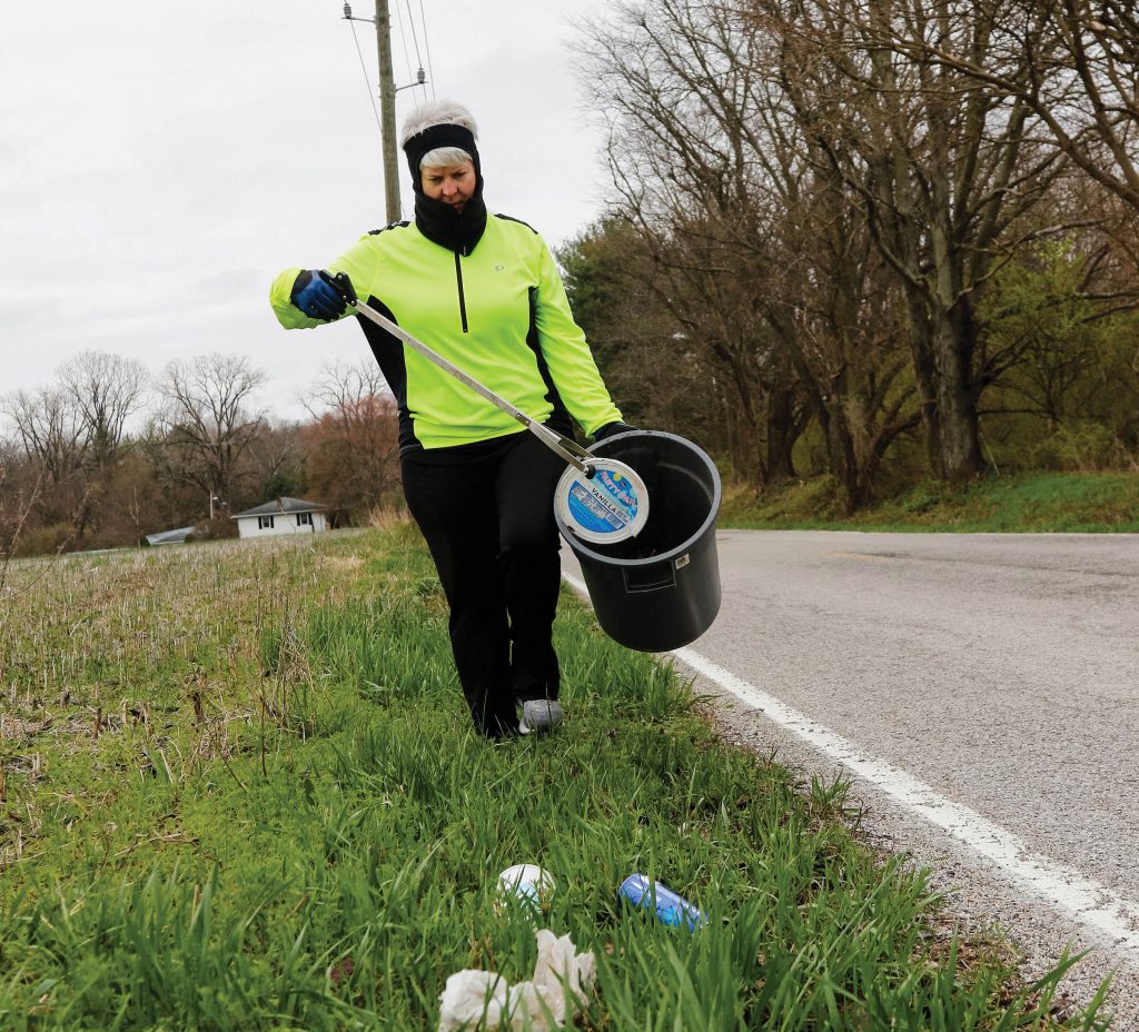 Photo of someone picking up trash along a roadside