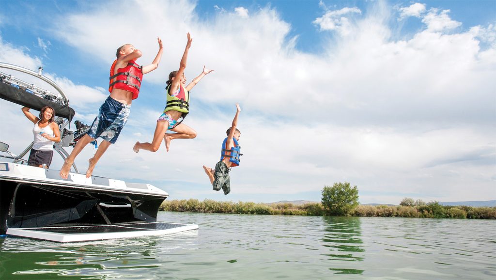 Kids jumping off the back of a boat into the water.