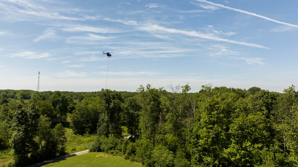 A helicopter-mounted aerial saw clears trees and brush from an electric transmission right-of-way as part of routine vegetation management.